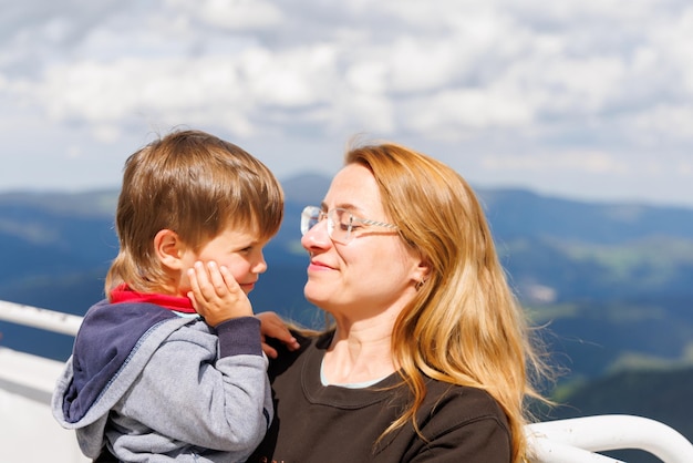La madre abraza a su hijo pequeño en la torre de observación en la cima de Snezhan contra el telón de fondo de las montañas Ródope y el cielo nublado