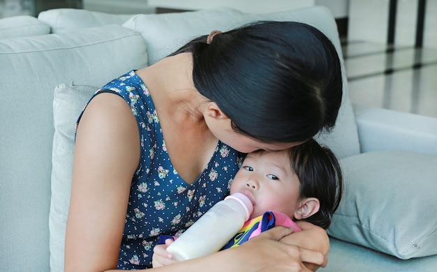 Madre abraza a su niña niño bebiendo de una botella en el sofá