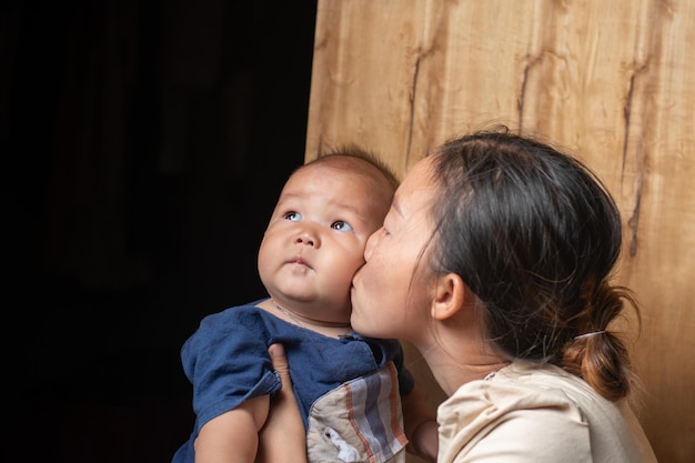 Una madre abrazando y besando a un bebé niño está mirando con luz fresca el concepto de relación entre madre e hijo, la paternidad y el recién nacido.