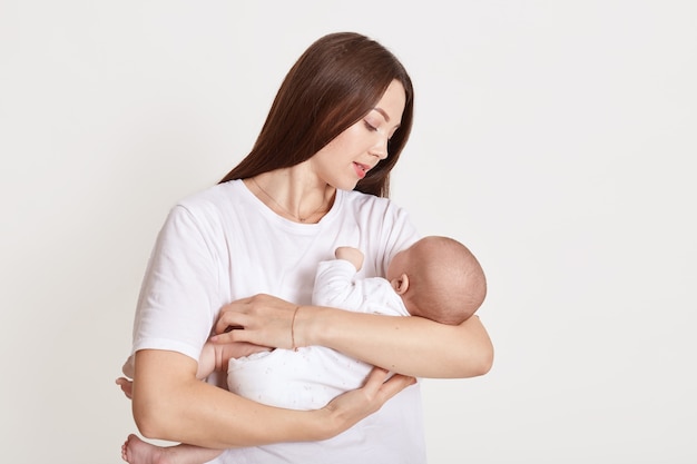 Madre abrazando a su hija recién nacida posando aislado sobre blanco