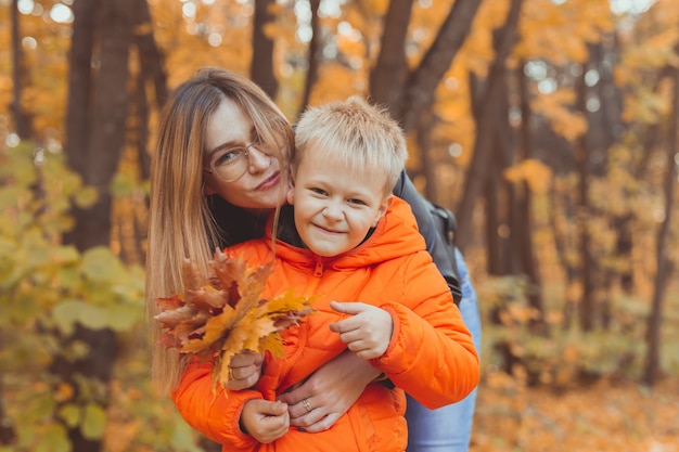 Madre abrazando a su hijo durante la caminata en el parque otoño temporada de otoño y concepto monoparental