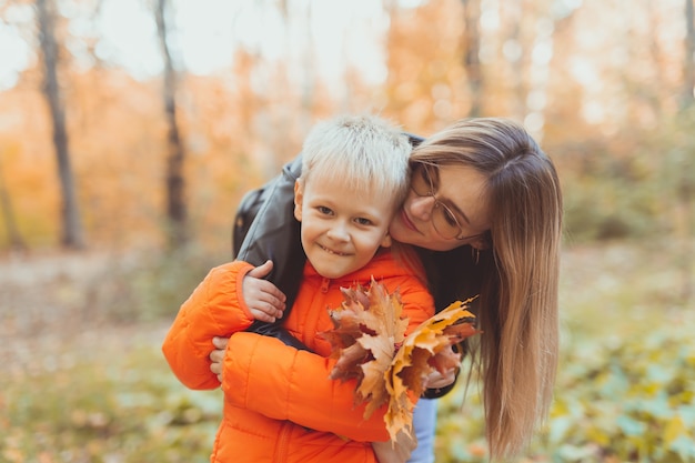 Madre abrazando a su hijo durante la caminata en el parque otoño temporada de otoño y concepto monoparental