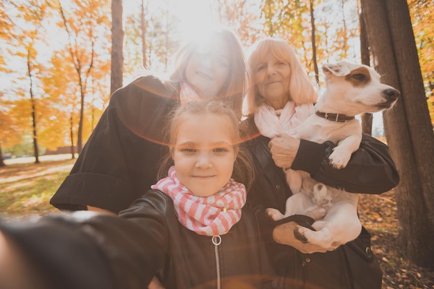 Madre, abuela y nieta con perro jack russell terrier tomando selfie por teléfono inteligente al aire libre en la naturaleza otoñal. Concepto de familia, mascotas y generación.