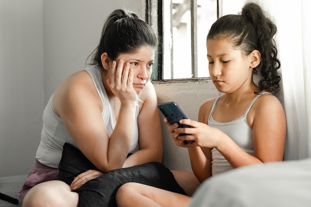 madre aburrida mirando a su hija con decepción porque no baja su teléfono celular