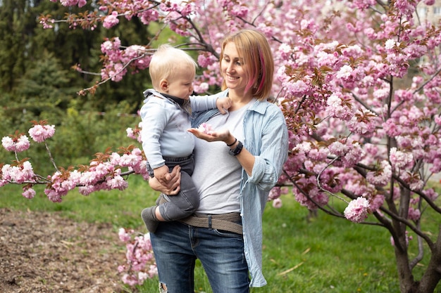 Madre con adorable hijo pequeño en el parque con Sakura Cherry Blossom Tree Feliz madre e hijo