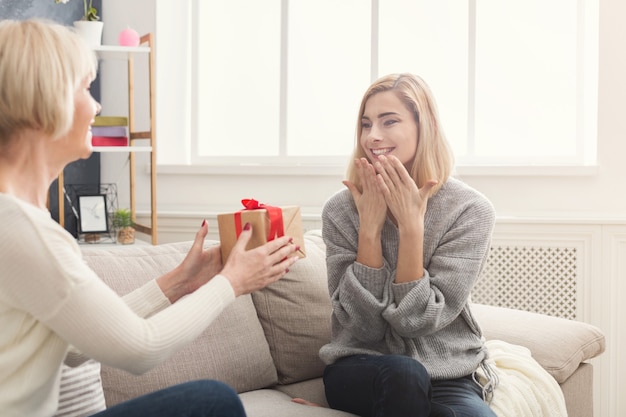 Madre adulta feliz dando presente a hija sorprendida. Pasar tiempo juntos, celebrar unas vacaciones en casa el fin de semana. Generación, relación, concepto de celebración, primer plano