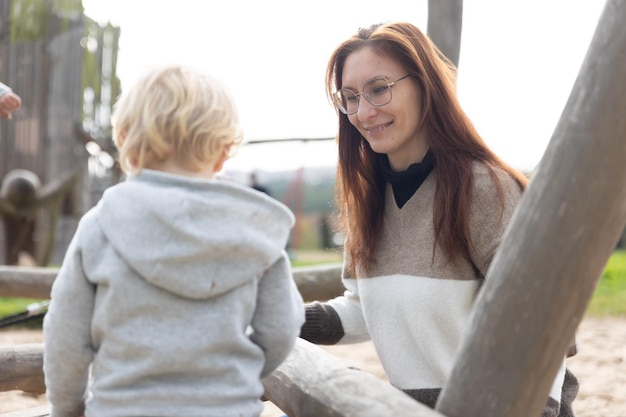 Madre adulta con gafas con su pequeño hijo en el patio de recreo