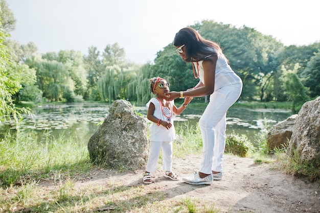 Madre afroamericana con hija en el lago de fondo de vestidos blancos en el parque