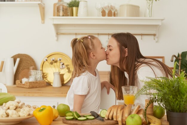 Madre alegre e hija pequeña están preparando ensalada juntos en la cocina y divirtiéndose.