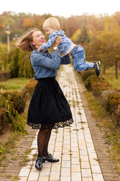 La madre alegre feliz que se divierte vomita en el niño del aire en parque del otoño.