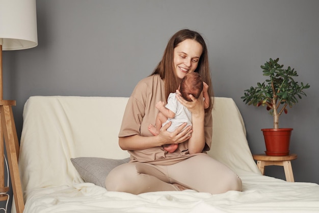 Una madre alegre y positiva sonriendo con un bebé recién nacido en las manos mirando a un niño pequeño jugando con su pequeña hija o hijo disfrutando de su maternidad