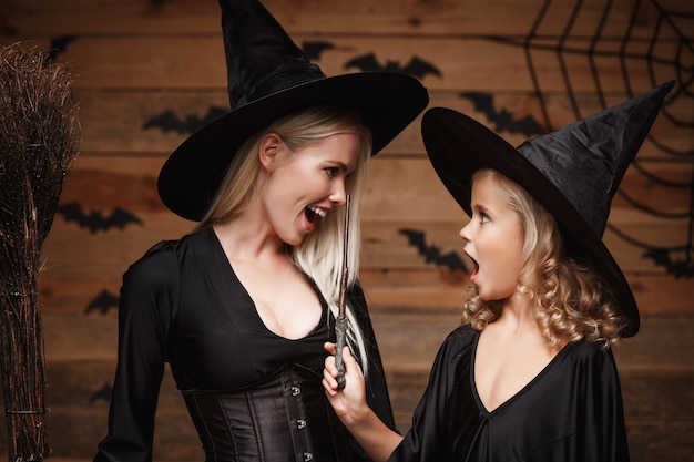 madre alegre y su hija en trajes de bruja que celebran la presentación de Halloween