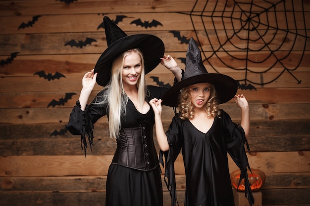 madre alegre y su hija en trajes de bruja que celebran la presentación de Halloween