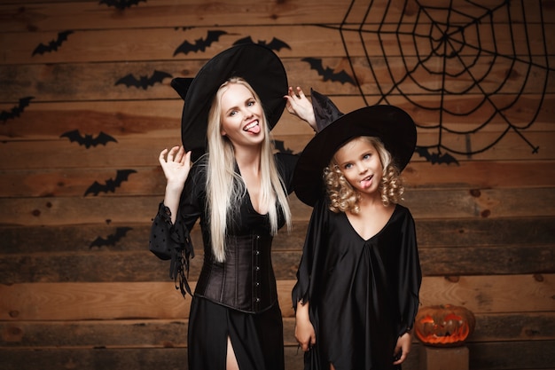 madre alegre y su hija en trajes de bruja que celebran la presentación de Halloween