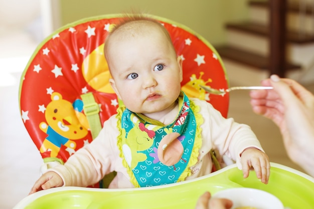 La madre alimenta a un bebé gracioso con una cuchara. niño come en una trona