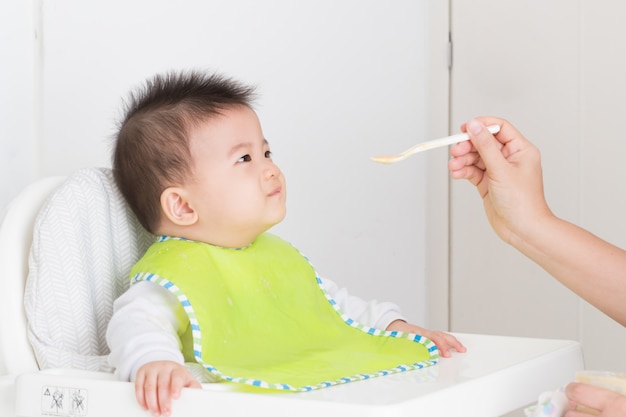 Madre alimentando comida para feliz bebé asiático bebé