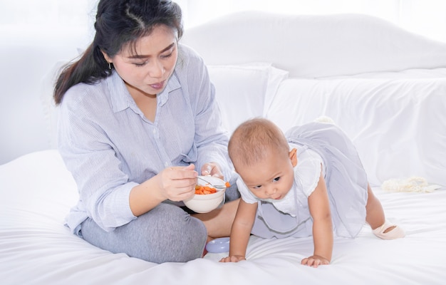 Madre alimentando frutas a su niña pequeña en la cama