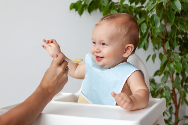 Madre alimentando lindo bebé rubio en babero azul de una cuchara