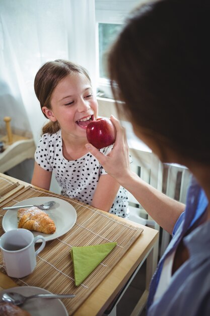 Madre alimentando manzana a su hija mientras desayuna