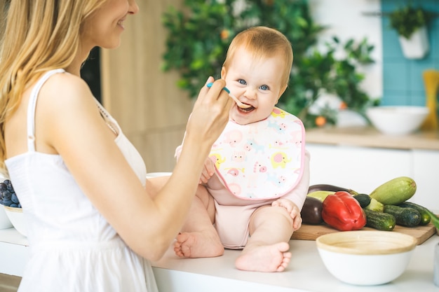 Foto madre alimentando a su bebé con una cuchara. madre dando comida a su adorable hijo en casa. comida para bebé