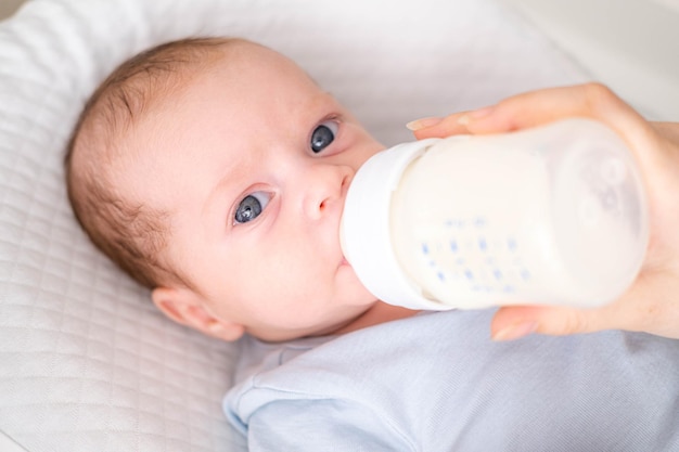 Madre amorosa alimentando a su niño pequeño con biberón de leche en casa retrato infantil Bebé comiendo bebiendo leche en polvo mirando a la cámara