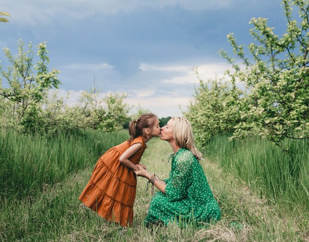 Una madre amorosa besa a su pequeña hija en los labios. Estoy en un jardín de primavera de manzano. relaciones familiares felices