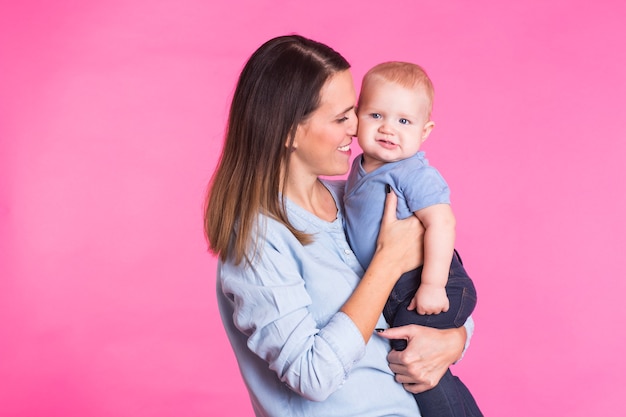 Madre amorosa jugando con su bebé en la pared rosa