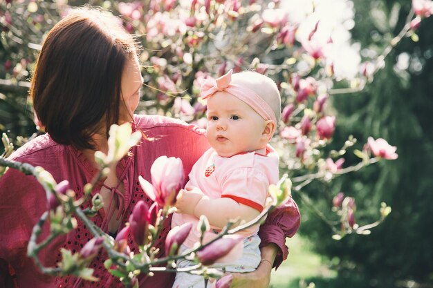 La madre amorosa y la niña huelen a flor de magnolia rosa floreciente Joven madre hermosa y pequeña hija entre flores de jardín al aire libre Familia en la naturaleza en Arboretum Eslovenia