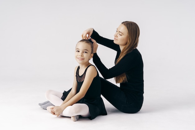 Madre anima a su hija bailarina sentada en el suelo en blanco