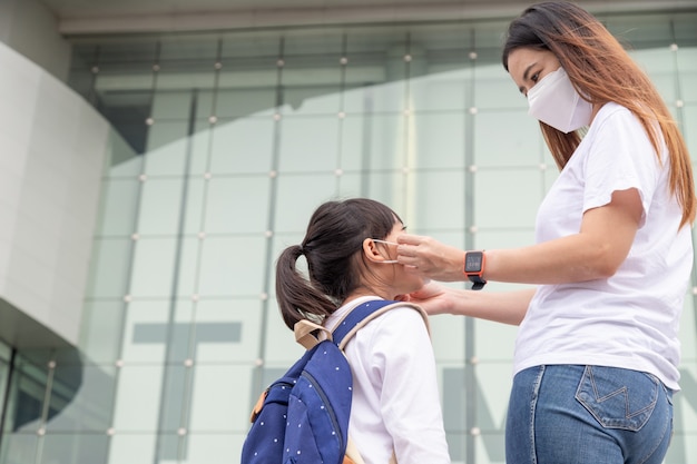 Madre asiática ayuda a su hija a usar una máscara médica para protegerse del brote de Covid19