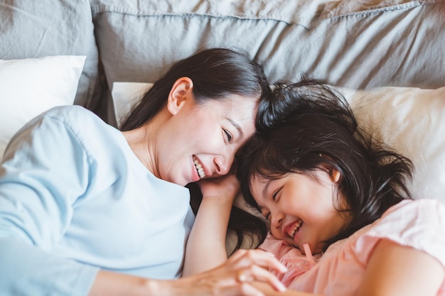 Madre asiática besando a su hija en el dormitorio con amor y un cálido concepto familiar