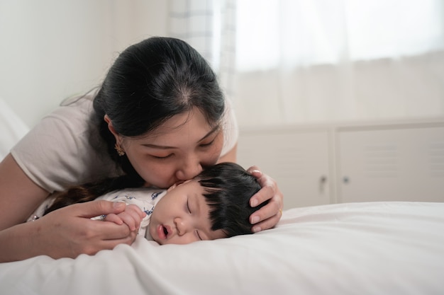 Madre asiática besando y tocando a un bebé que duerme en la cama con cariño