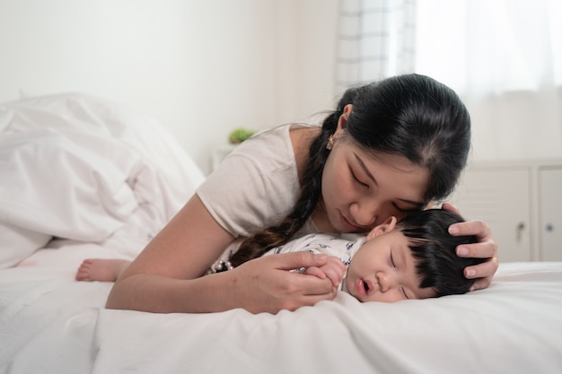 Madre asiática besando y tocando a un bebé que duerme en la cama con suavidad y amor, sintiéndose feliz.