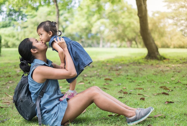 Madre asiática e hija jugando y besándose juntos en el parque verde