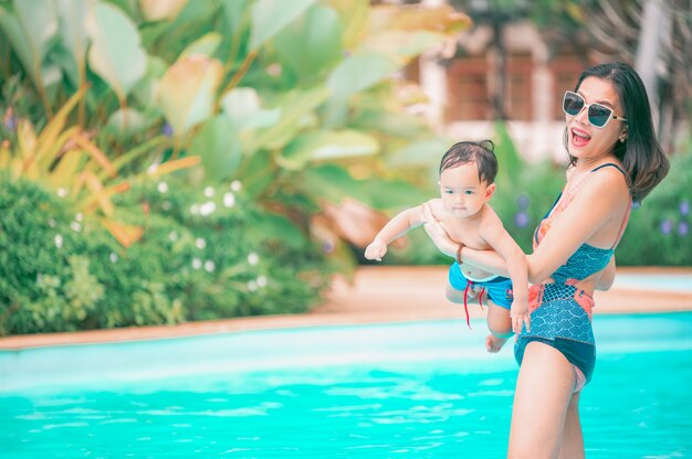 Madre asiática e hijo pequeño disfrutando de nadar en una piscina en vacaciones de verano.