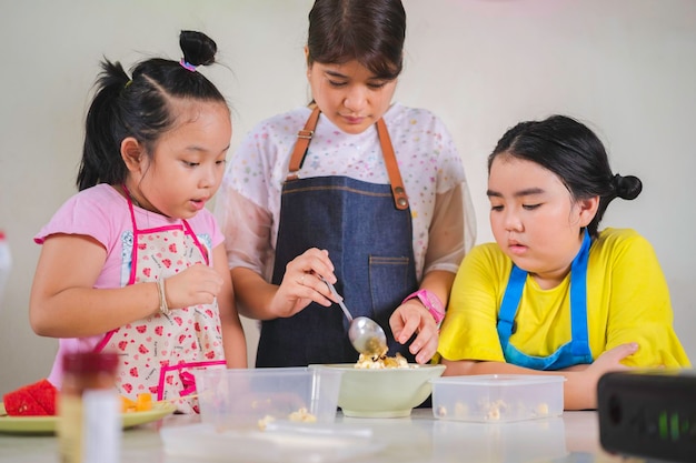 Madre asiática enseñando a su hija a aprender a hacer palomitas de maíz en la cocina de la vida real en casa