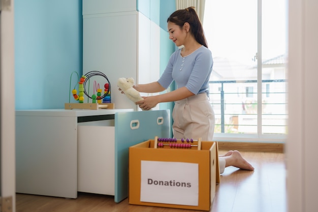 La madre asiática está eligiendo los juguetes de sus hijos que no están jugando y poniendo cajas de donación en el centro de donación.