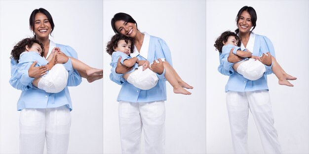 La madre asiática y la hija caucásica se ponen de pie y visten juntas el mismo pantalón azul. La niña toma la mano de mamá y sonríe con amor. Fondo blanco aislado