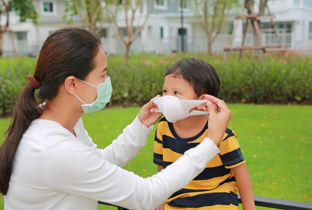 Madre asiática con mascarilla protectora para bebé en el jardín público durante el brote de coronavirus y gripe