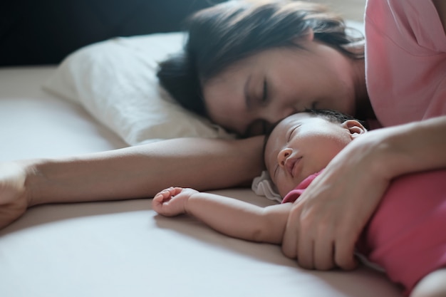 Madre asiática que abraza a su bebé recién nacido que duerme en cama.