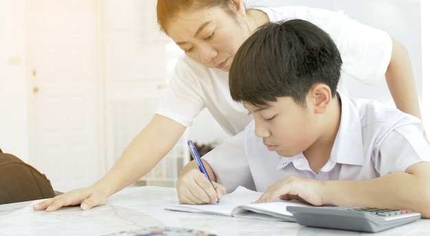 Madre asiática que ayuda a su hijo que hace la preparación en la tabla blanca.