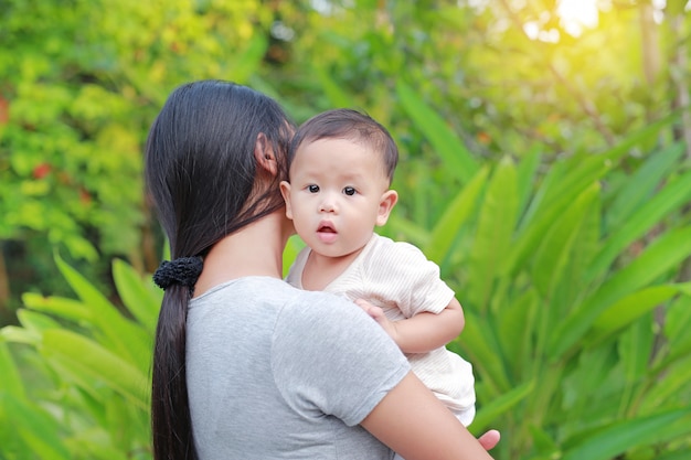 Madre asiática que lleva a su bebé infantil en el jardín verde.