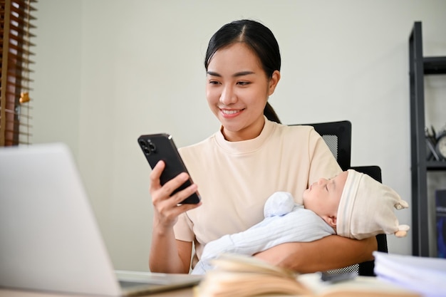 Una madre asiática que trabaja desde casa hablando por teléfono y sosteniendo a su bebé con los brazos