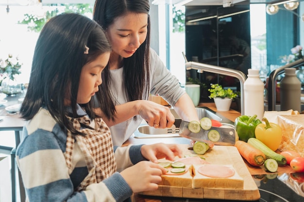 Madre asiática y su hija cocinando comida para el desayuno en la cocina