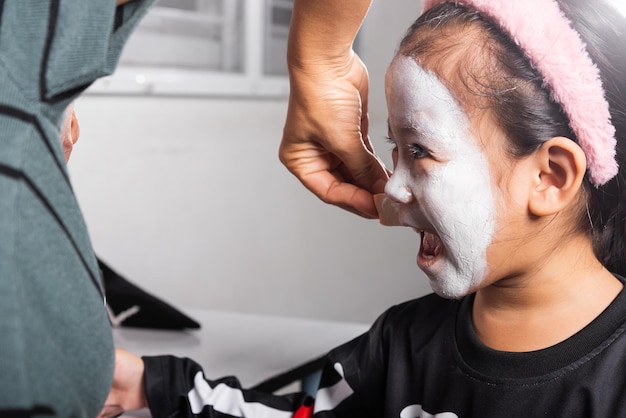 Madre asiática y su hija maquillada pintan caras de halloween como un fantasma