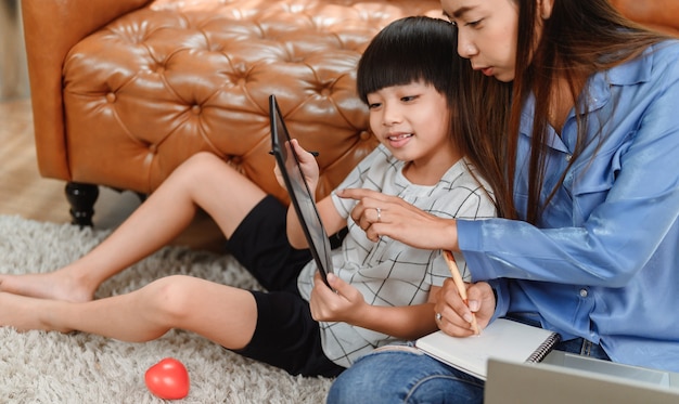 Madre asiática trabaja en casa junto con su hijo. Mamá enseñando al niño para la educación de aprendizaje en línea. Nuevo estilo de vida normal y actividad familiar.