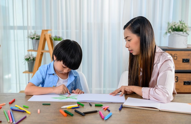 Madre asiática trabaja en casa junto con su hijo. Mamá y niño dibujando imagen y pintura en color. Estilo de vida de mujer y actividad familiar.