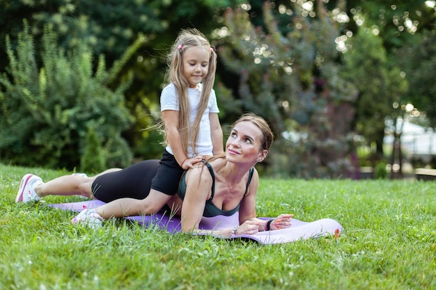 La madre atlética con la hija en la espalda está practicando ejercicios de tabla en el parque pasan tiempo juntos familia saludable