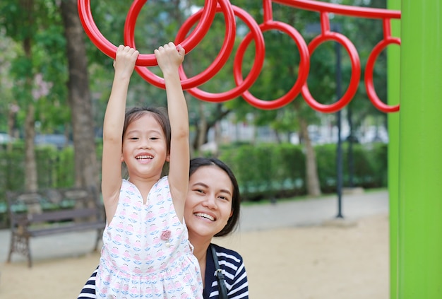 Madre ayuda a su hija a jugar en el anillo de gimnasia en el patio al aire libre.