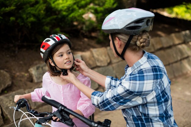 Madre ayudando a la hija a usar casco de bicicleta en el parque